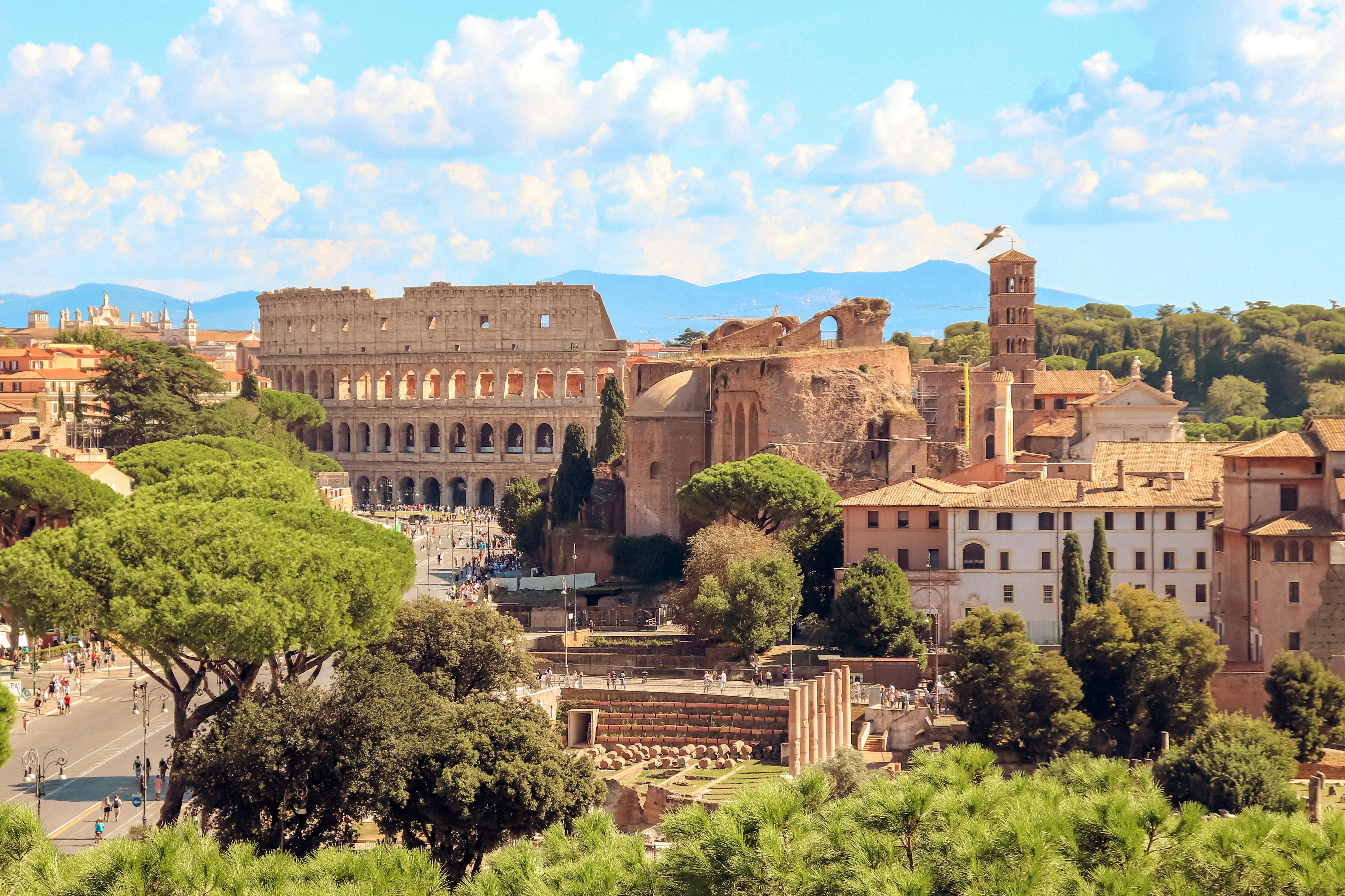 The Colosseum at golden hour with the Roman Forum and umbrella pines in the foreground, mountains visible behind — the urban texture that makes Rome a multi-week stay candidate.