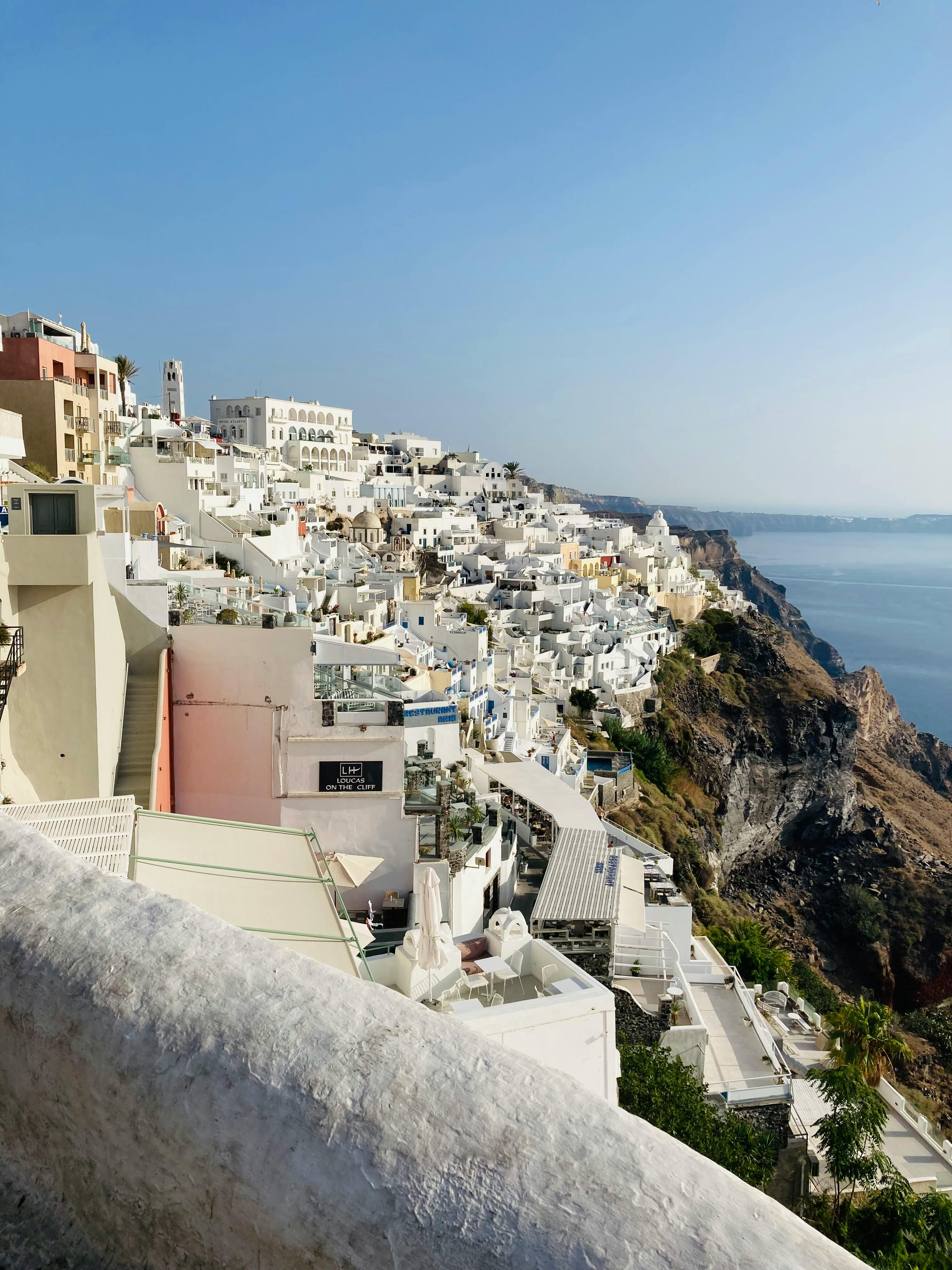 A view of Santorini's whitewashed buildings against the deep-blue Aegean Sea, bathed in bright Mediterranean light.